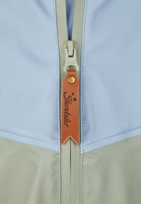 Jacke mit Reißverschluss, die einen hellblauen oberen Stoff und einen hellgrünen unteren Stoff hat. Enthält einen Leder-Reißverschluss-Zipper mit eingestanztem Text und Sternen.