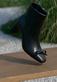 Bottines noires en cuir lisse, avec un bout pointu et un petit accent de nœud à l'avant. Le talon est de hauteur moyenne.
