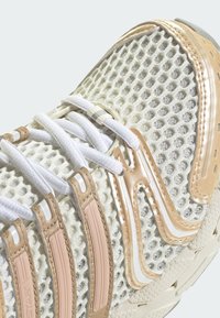 Viegls sporta apavi ar acu sietu augšdaļu krēmkrāsā, ar bežiem un baltiem sintētiskiem svītrām un plakanu balto auklu. Gumijas zole.