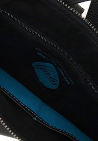 Interno nero di una borsa con rivestimento blu, una cerniera visibile e un'etichetta con il marchio che indica "Made in Italy".