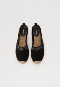 Espadrilles en toile noire à enfiler avec une semelle extérieure en jute texturé, présentant une bande de logo contrastante et un design minimaliste.