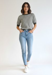 Czarnobiały dzianinowy top w kratkę z krótkimi rękawami, zestawiony z jasnoniebieskimi dopasowanymi jeansami i białymi tenisówkami. Prosty, codzienny strój.