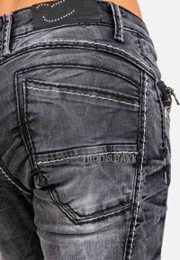 Jeans in denim grigio con cuciture bianche a contrasto, molteplici tasche e un logo visibile sul retro. Tessuto testurizzato con leggere sfumature.