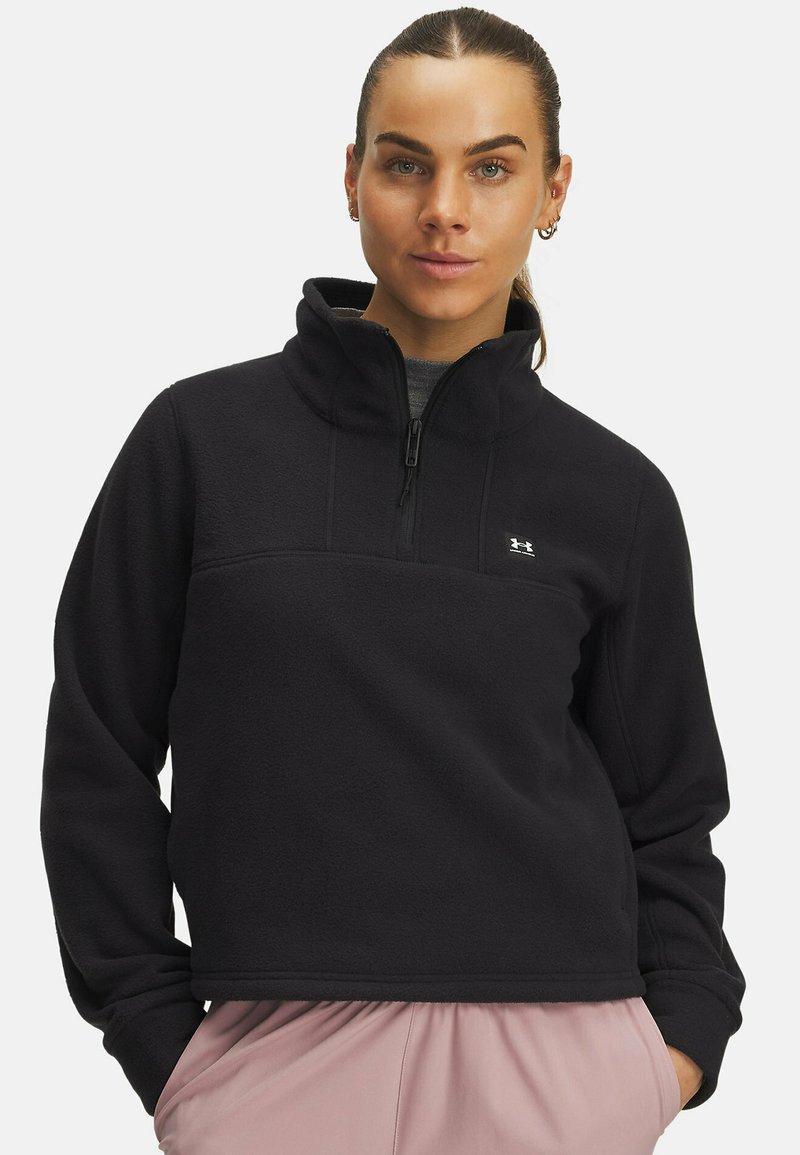 Mustavilla fleece-huppari, jossa on puolivetoketju kauluksessa, teksturoitu pinta ja pieni logo rinnassa. Muotoilu on lyhennetty ja rento istuvuus.