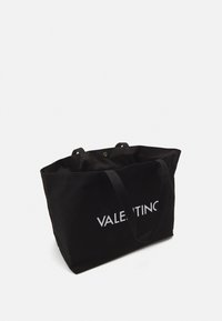 Svart canvas tote-väska med två handtag, som har en kontrasterande vit logotyp. Designen är enkel, med öppen topp och synligt innandöme.