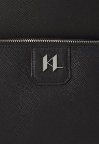 Black textured leather bag featuring a silver zip closure and a rectangular tag with embossed logo detail.
