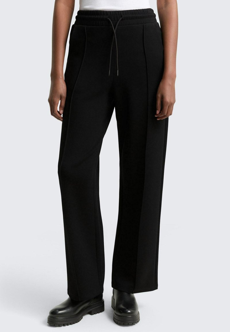 Schwarze Sweatpants mit lässiger Passform, ausgestattet mit einem elastischen Bund mit Kordelzug, vorderen Falten und subtilen seitlichen Akzenten. Tragen mit schwarzen Plattformstiefeln.