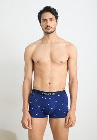 Boxers bleus en tissu extensible, avec une ceinture noire à logo de la marque et des motifs blancs sur l'ensemble. Texture douce.