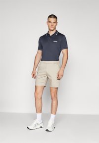 Jūras spēku polo krekls ar baltām akcents, beicēti šorti un balti sporta apavi. Krekls ir ar zīmola logo; šorti ir ikdienišķi un pieguļoši.