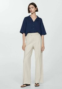 Navy short-sleeve shirt with a collar and buttons paired with high-waisted beige wide-leg trousers. Flat sandals complete the look.