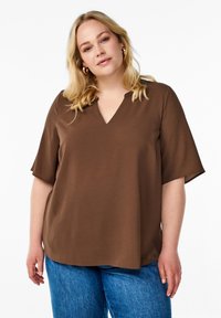 Haut court marron à manches courtes avec un col en V, fabriqué en tissu texturé, présentant une coupe décontractée et un ourlet arrondi, associé à un jean bleu.