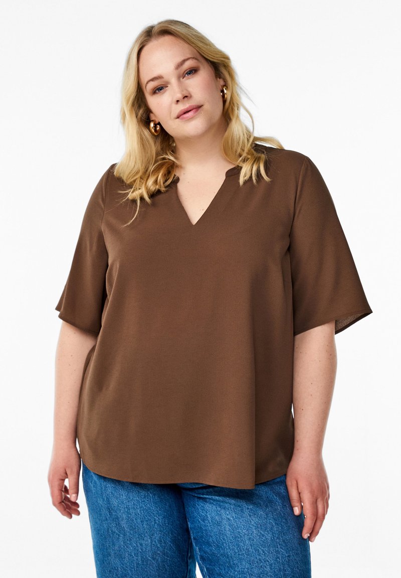 Haut court marron à manches courtes avec un col en V, fabriqué en tissu texturé, présentant une coupe décontractée et un ourlet arrondi, associé à un jean bleu.