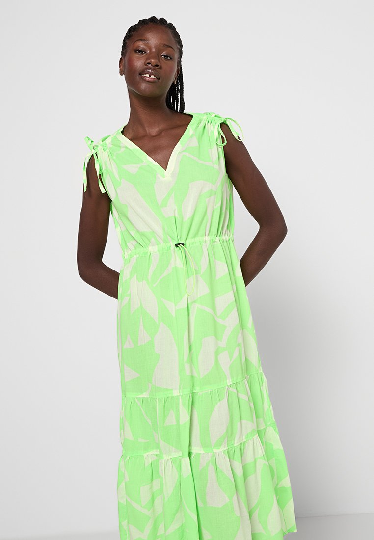 Zielona sukienka z dekoltem w serek, ozdobiona białym abstrakcyjnym wzorem. Regulowane sznurki na ramiączkach, sukienka z warstwami i marszczona talia dla luźnego dopasowania.