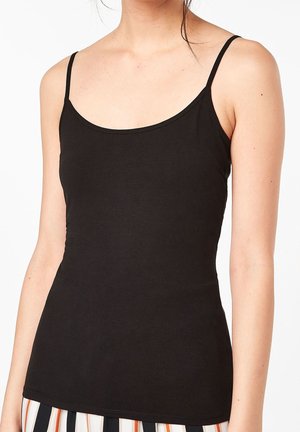 Kobieta nosząca dopasowany czarny top bez rękawów z cienkimi ramiączkami i okrągłym dekoltem, w zestawieniu z pasiastymi spodniami, na białym tle.