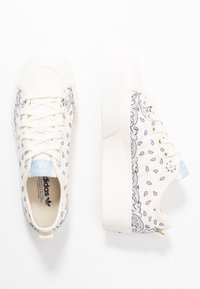 Vita kanvas sneakers med ett paisleymönster, beige detaljer, platta snören och en vit gummisula. Logotyp på tungan i ljusblått.