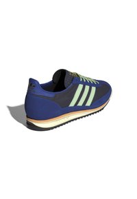 Pantofii sport albaștri și verzi cu țesătură texturată, trei dungi verzi și guler căptușit. Talpă din cauciuc cu o ușoară înălțare.