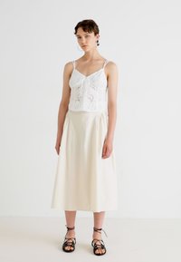 Hvit broderte crop top med et dekorativt design, kombinert med et beige A-line skjørt. Brukt med svarte sandaler med stropper.