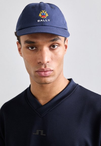 Marineblå baseballcap med broderet Bally-logo og -våben, parret med en struktureret sort v-hals skjorte med en subtil logoaccent.