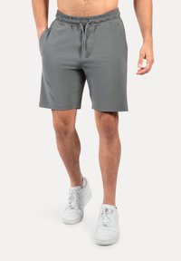 Grijze sportbroek met een elastische tailleband en trekkoord, voorzien van zijzakken en een gladde textuur. G gedragen met witte sneakers.