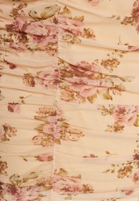 Tissu froncé dans un doux pêche avec de délicats motifs floraux roses et bruns. Tissu texturé avec des coutures visibles le long des seams.