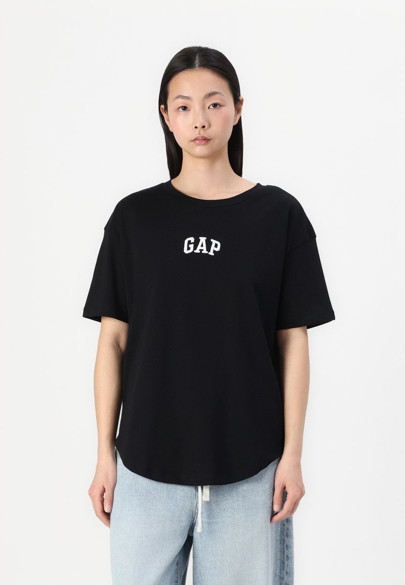 Svart kortermet t-skjorte med rund hals, med hvit "GAP" logo på brystet. Laget av mykt stoff med en avslappet passform.
