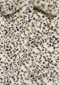 Fuskepelsjakke i cremefarve med sorte leopardpletter. Har lynlås som lukning og en blød, tekstureret overflade. Kravedesign tilføjer visuel interesse.