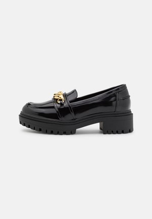 Mocassin noir brillant avec semelle épaisse à crampons et petit talon bloc, avec un détail chaîne dorée sur le dessus.