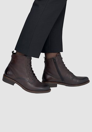 Brown leather ankle boots with side zippers and laces worn with black cropped pants on a light gray background.
