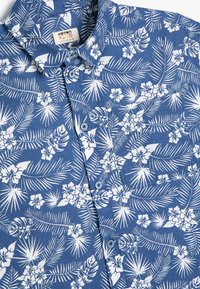 Niebieska koszula z krótkim rękawem w białe kwiatowe i palmowe wzory, z zapięciem na guziki z przodu i klasycznym kołnierzykiem. Miękki, fakturowany materiał.