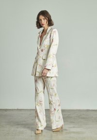 Bloemmotief pak in lichte stof; beschikt over een gestructureerde blazer met notch revers en wijde broekspijpen. Kleuren zijn pastelroze en groen.