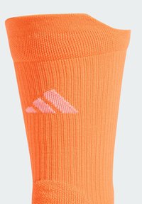 Calcetín atlético naranja con textura acanalada y un logo de Adidas en rosa. El borde superior tiene un puño reforzado para mayor durabilidad.