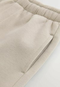 Light beige pants with a smooth texture, featuring an elastic waistband and side pockets. Simple design, no patterns or hardware visible.