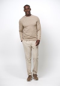 Suéter de punto beige con cuello redondo, combinado con pantalones texturizados beige claro y zapatillas marrones con cordones. Diseño minimalista.