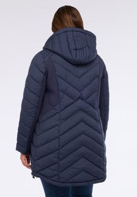 Abrigo puffer náutico con patrón de rombos, capucha y paneles laterales. Presenta un cierre con cremallera y dobladillo ajustable para un mejor ajuste. Tela suave e aislante.
