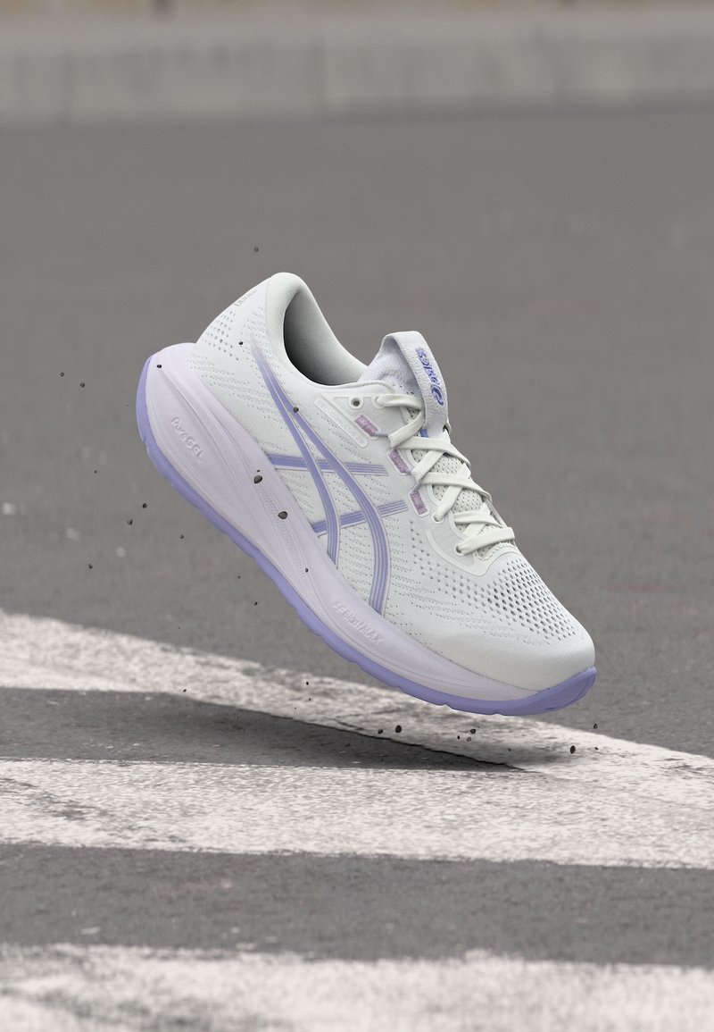 Άσπρο και ανοιχτό μοβ παπούτσι για τρέξιμο στον αέρα πάνω από άσφαλτο με λευκές διαγραμμίσεις δρόμου, μικρές πέτρες που πετάχτηκαν γύρω από την σόλα.