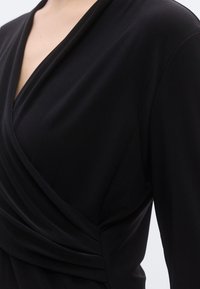 Zwarte top in wikkelstijl met gedrapeerde stof, voorzien van een diepe V-hals en lange mouwen, gemaakt van een gladde, elastische stof.