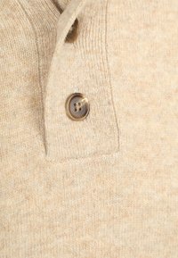 Close-up van beige gebreide stof met twee bruine knopen met vier gaten genaaid op een sluiting.