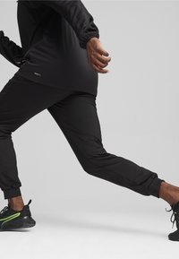 Svarta träningsbyxor i en avsmalnande design med elastiska muddar. Tyget ser slätt ut med en lätt lyster. Märket syns tydligt på sidan.