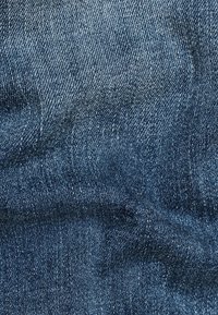 Denimtyg i nyanser av blått med en vävd textur, som har subtila färgvariationer och ett mjukt, något nött utseende.