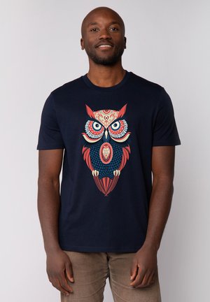 Donker marineblauwe t-shirt met een gedetailleerde, kleurrijke uilafbeelding met ingewikkelde patronen, grote ogen en veeraccenten. Korte mouwen.