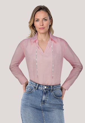 Helles Pinkes Blusenshirt mit Kragen, langen Ärmeln und V-Ausschnitt. Verfügt über einen Kordelzug und wird mit einem Jeansrock kombiniert. Weicher, transparenter Stoff.