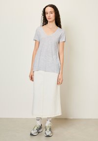 Šviesiai pilkas v-kaklo marškinėliai su trumpomis rankovėmis, derinami su baltais džinsiniais sijonais. Dėvimi su pilkais sportiniais bateliais ir baltais kojiniais, ant kurių yra tekstas.