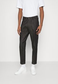 Svarta jeans med en avslappnad passform, justerbart midjeband och framfickor, i kombination med vita sneakers och en vit t-shirt.