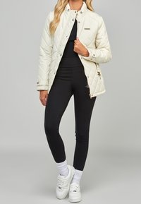 Vadderad gräddvit jacka med tryckknappar och hög krage, kombinerad med svarta leggings och vita sneakers, med ribbade mudd och ankelsockor.