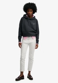 Sort bomulds hoodie med snøre, logodetalje, lagdelt over en lyserød skjorte. Sammen med hvide jeans med lige ben og bordeaux loafers.