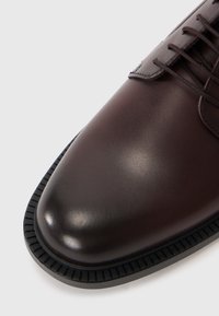 Chaussure habillée en cuir brun avec une surface lisse, un bout arrondi et une semelle en caoutchouc texturé contrastante. Lacets pour un ajustement sécurisé sur le dessus.