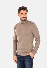 Maglione beige a collo alto in un morbido tessuto a maglia, con maniche lunghe e polsini a coste, abbinato a jeans blu scuro.