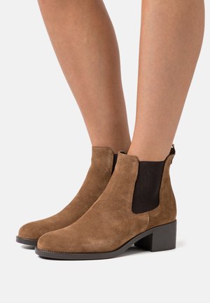 Bottes de cheville en suede marron avec des panneaux élastiques sur les côtés, un bout arrondi et un faible talon bloc. Finition texturée avec un minimum de détails.
