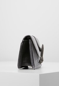 Borsa a mano in velluto grigio con una forma strutturata, dotata di un manico a catena metallica decorativa e una chiusura magnetica. Texture liscia e design minimalista.