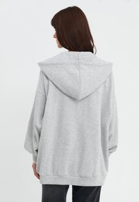 Haut à capuche oversize gris avec une capuche pointue et un ourlet côtelé. Tissu doux, coupe décontractée, avec des coutures d'épaules tombantes. Design simple et minimaliste.